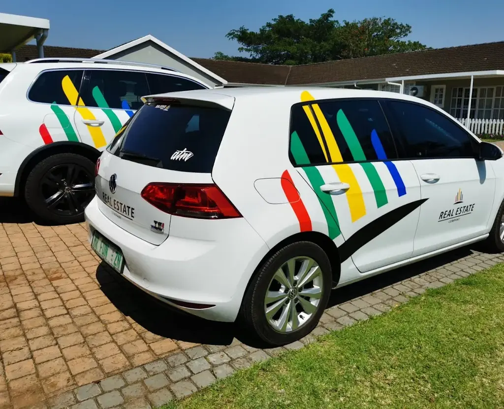 White Volkswagen Golf hatchback featuring colourful red, yellow, green and blue diagonal vinyl graphics on its rear windows and side panels.