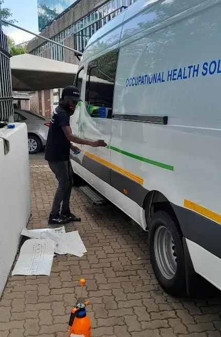 Professional installer applying green vinyl graphics to a white Mercedes-Benz Sprinter minibus featuring Occupational Health Solutions company lettering.