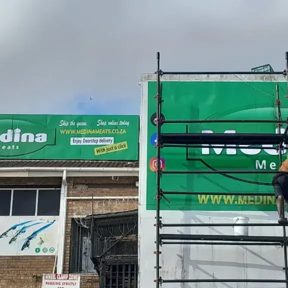 Professional exterior retail signage featuring coordinated green branding across storefront and elevated advertising structures.